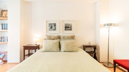Chambre lumineuse d'un appartement à Porto avec lit crème, tables de nuit en bois, œuvres d'art encadrées et étagères à Flowerstreet54