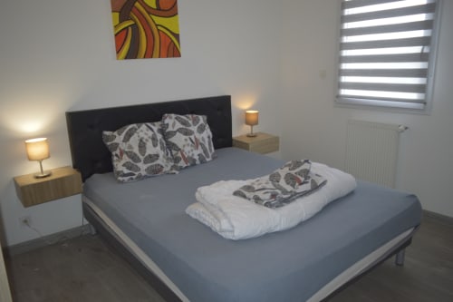 Chambre moderne à la Résidence des dunes à Landéda avec lit gris, tête de lit noire, tables de nuit en bois et art mural coloré