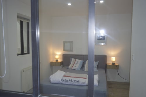 Chambre moderne de la Résidence des Dunes à Landéda avec lit double, tête de lit grise, lampes de chevet et miroir.