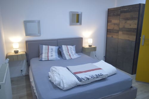 Chambre moderne à la Résidence des dunes, Landéda avec lit queen-size, literie grise, armoire en bois, lampes de chevet et porte jaune.