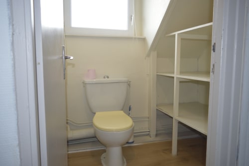 Salle de bain avec toilettes, siège jaune et étagères blanches à la Résidence des dunes, Landéda