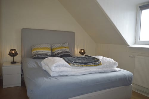Chambre mansardée lumineuse à la Résidence des dunes, Landéda avec lit queen-size, tête de lit grise, oreillers jaunes et fenêtre de toit
