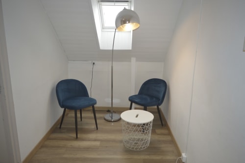 Coin salon moderne à la Résidence des dunes, Landéda avec deux chaises bleues, table d'appoint blanche, lampadaire arc et puits de lumière