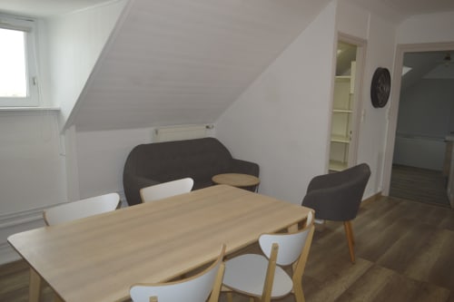 Salle à manger lumineuse dans un appartement mansardé à la Résidence des dunes, Landéda, avec table en bois et sièges modernes