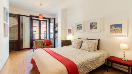 Romantic Porto apartment bedroom with city view, queen bed, balcony doors, hardwood floors, and framed cityscape photos