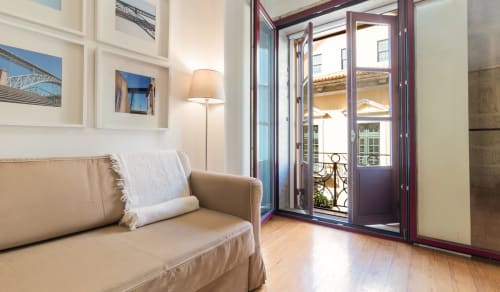 Canapé beige avec coussin blanc dans le salon d'un appartement à Porto, portes ouvertes donnant sur un balcon avec vue sur la ville