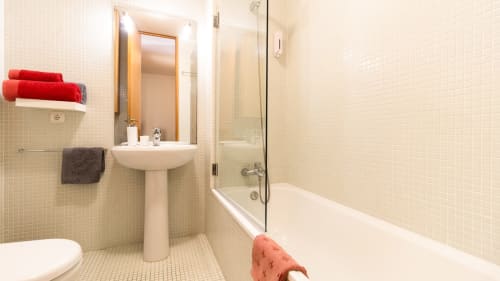 Salle de bain moderne de l'appartement Flowerstreet54 Porto avec lavabo sur piédestal, baignoire, cabine de douche en verre et serviettes rouges