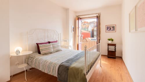 Bright bedroom with white iron bed, striped bedding, wooden floors, and open balcony door overlooking Porto city view at
