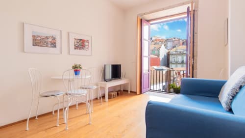Séjour moderne d'un appartement portuense avec canapé bleu, table à manger, téléviseur et balcon donnant sur les bâtiments historiques de la ville