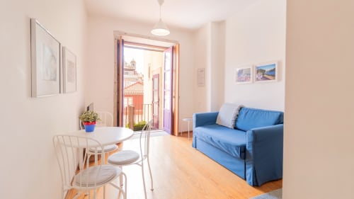 Lumineux séjour à Porto avec canapé bleu, table à manger, parquet et vue sur la ville depuis le balcon près de la gare