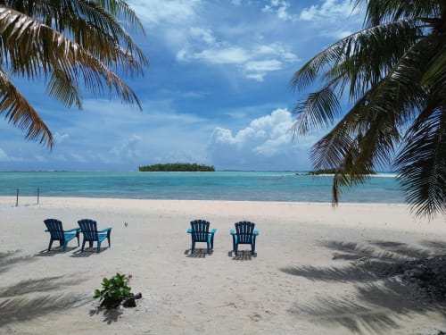 Chaises Adirondack bleues sur sable blanc, lagon turquoise et palmiers à Tikehau Herearii, Polynésie française