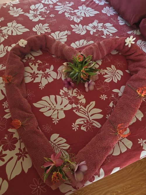 Arrangement de serviette en forme de cœur avec fleurs fraîches sur literie fleurie à Tikehau Herearii, Tuherahera