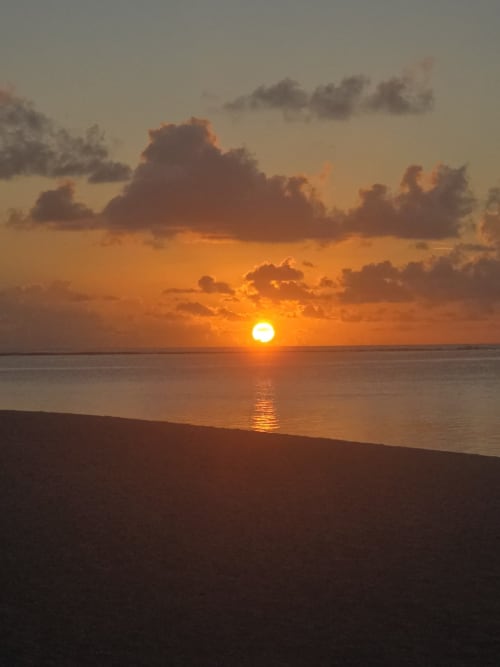 Coucher de soleil doré sur l'océan à Tikehau Herearii à Tuherahera avec nuages et plage de sable