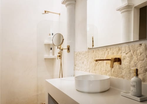 Modern bathroom at Villa Merida Boutique Hotel with white vessel sink, gold fixtures, and natural stone backsplash in Merida