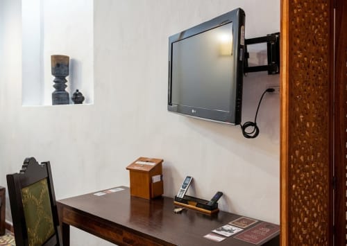 Modern hotel room desk with wall-mounted flat-screen TV, wooden furniture, and remote controls at Villa Merida Boutique Hotel