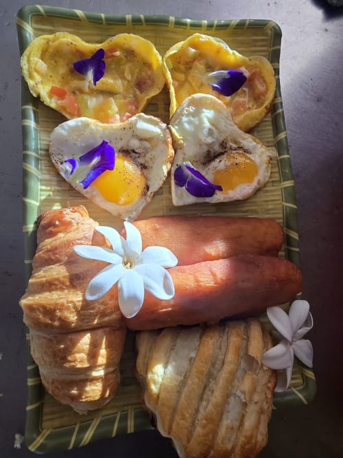 Gourmet breakfast platter at Tikehau Herearii with pastries, eggs, sausage, and edible flowers in Tuherahera