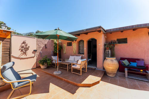Terrazza soleggiata a Villa Verde con edificio dipinto di arancione, ombrellone verde, arredo in legno e vista sul giardino