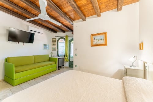 Camera ospiti luminosa a Villa Verde con divano verde lime, travi in legno a vista e letto confortevole con vista sul giardino a Torre