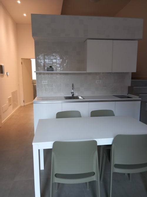 Cucina e zona pranzo moderna della camera dell'Albergo Giulia Gonzaga di Sabbioneta, con mobili bianchi e sedie verdi
