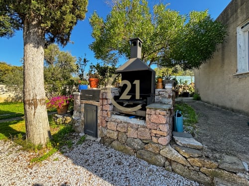 Four à bois noir numéroté 21 au jardin de la villa L'Île-Rousse, entouré d'arbres et de pots en terre cuite
