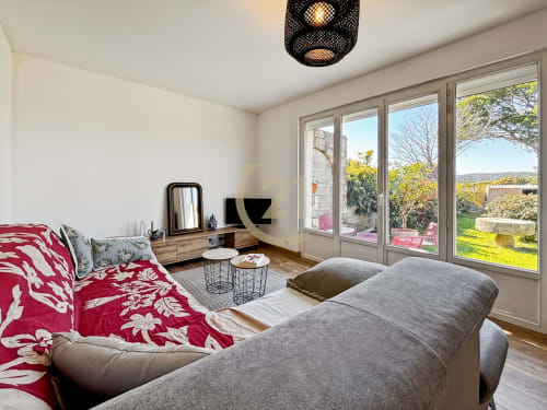 Chambre moderne de villa à L'Île-Rousse avec vue jardin, literie rouge, canapé gris, bureau et grandes portes-fenêtres donnant sur