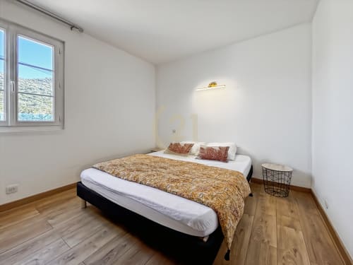 Chambre lumineuse aux planchers de bois, lit queen, literie dorée et vue sur le jardin dans la villa de L'Île-Rousse
