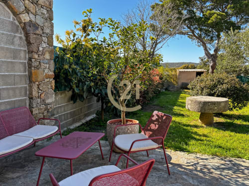 Terrasse de jardin pittoresque de la villa Lozari à L'Île-Rousse avec sièges bordeaux, plantes en pot et éléments en pierre