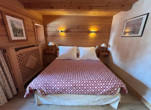 Cozy wooden chalet bedroom with queen bed, white pillows, patterned burgundy bedding, wooden nightstands, wall sconces, and