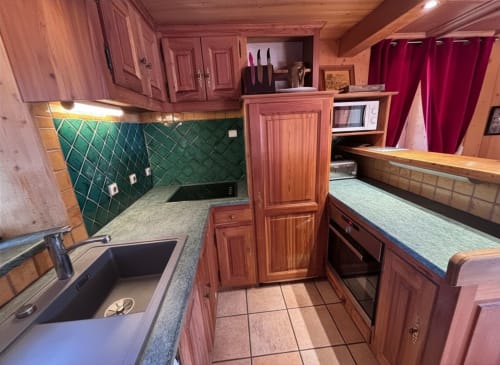 Chalet Marie Claire kitchen with wooden cabinetry, green tile backsplash, and stainless appliances in Notre Dame de