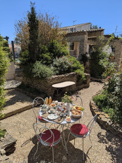 Table de petit-déjeuner avec chaises bordeaux dans le jardin-cour en pierre de La Closerie, La Redorte France