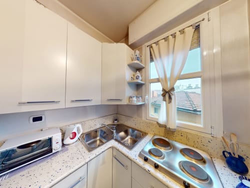 Moderne Küche im Apartment Marghera Home Milano mit weißen Möbeln, Induktionskochfeld und Stadtblick durch großes Fenster