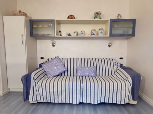 Gemütliches Apartment-Schlafzimmer in Milano mit gestreiftem Sofa, blau-weißer Dekoration, Wandregalen und Stauraum.