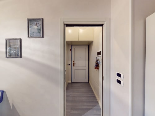 Moderner Eingangsbereich des Apartments Come a Casa Tua in Mailand mit weißen Wänden, gerahmten Kunstwerken und Zugang zur Haupttür