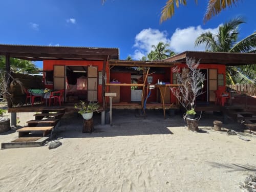 Bungalow rouge de plage à Tikehau Herearii à Tuherahera avec palmiers et sol sablonneux