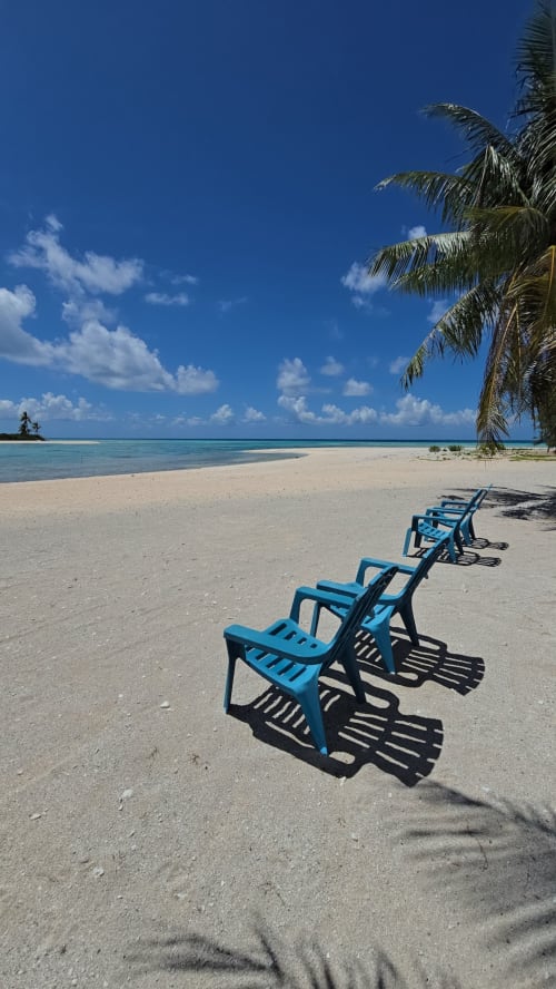 Blue lounge chairs on sandy beach with palm tree and turquoise lagoon at Tikehau Herearii, French Polynesia