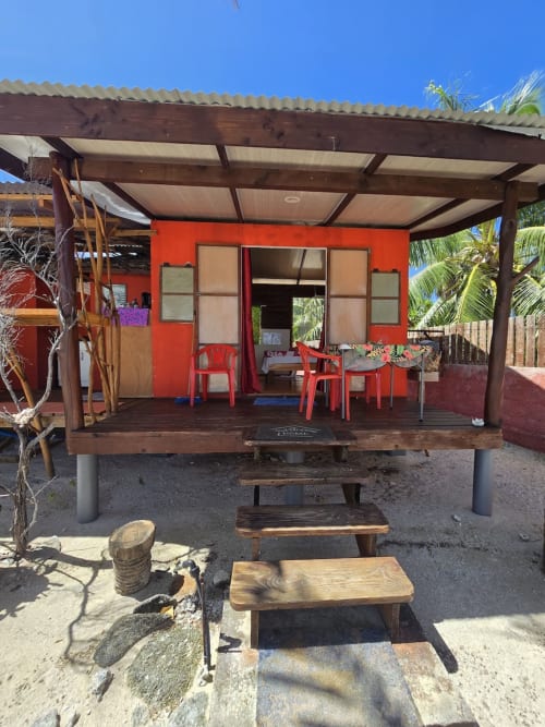 Bungalow rouge au Tikehau Herearii avec terrasse en bois, patio couvert, chaises rouges et vue sur la plage à Tuherahera, Polynésie française