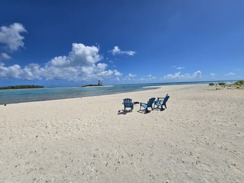 Three blue Adirondack chairs on pristine white sand beach at Tikehau Herearii, Tuherahera with turquoise lagoon and blue sky