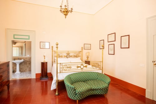Camera elegante a Villa Ceci ad Andria con letto in ottone ornato, divano verde decorativo e pavimenti in cotto rosso