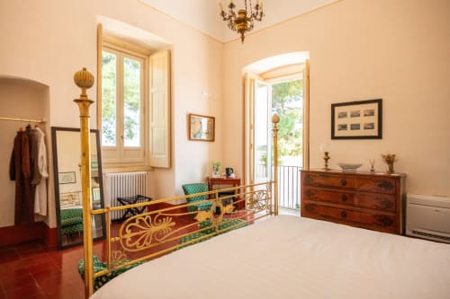 Elegante camera da letto a Villa Ceci in Andria con letto ornato, cassettiera in legno e vista sul giardino attraverso le porte francesi