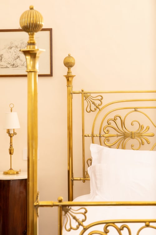 Elegante letto in ottone con testata ornamentale e biancheria bianca nella suite King Deluxe di Villa Ceci, Andria