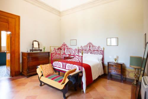 Elegante camera da letto a Villa Ceci con letto in ferro rosso ornamentale, mobili in legno e pavimento in cotto ad Andria, Italia