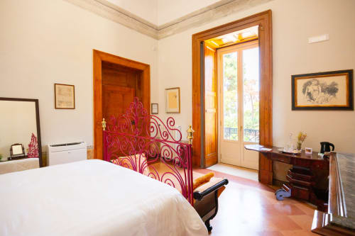 Elegante suite junior con letto in ferro battuto rosso ornato, porte in legno, vista sul giardino e stile classico italiano