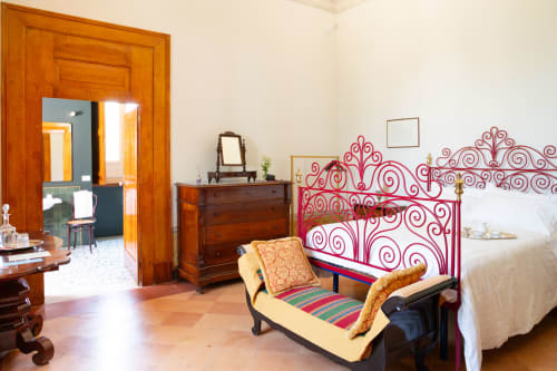 Camera Vittoria Junior Suite a Villa Ceci ad Andria con letto in ferro rosso ornato, mobili in legno e vista sul giardino