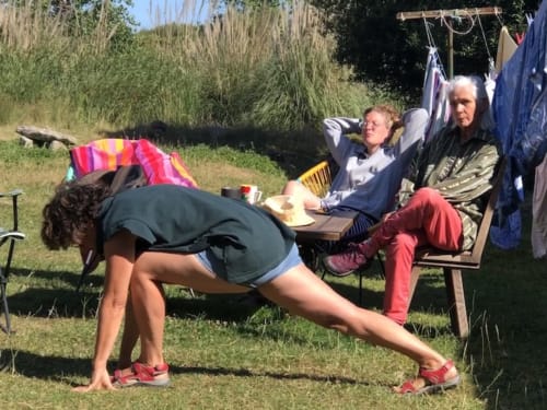 Frau beim Yoga im B&B Le Lama Zébré in Penmarch, Frankreich, während Gäste von Stühlen im Freien zuschauen.