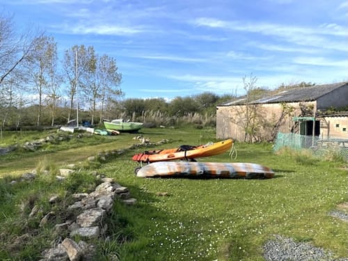 Bunte Kajaks auf einer Wiese in der Unterkunft Le Lama Zébré in Penmarch, Frankreich, mit Booten und Landblicken.