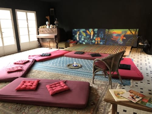 Colorful meditation room at Le Lama Zébré in Penmarch with pink cushions, woven bed, tropical artwork.