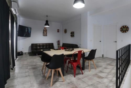 Sala común moderna de apartamento en Mérida con mesa de comedor, sillas rojas, sofás negros, TV e iluminación industrial