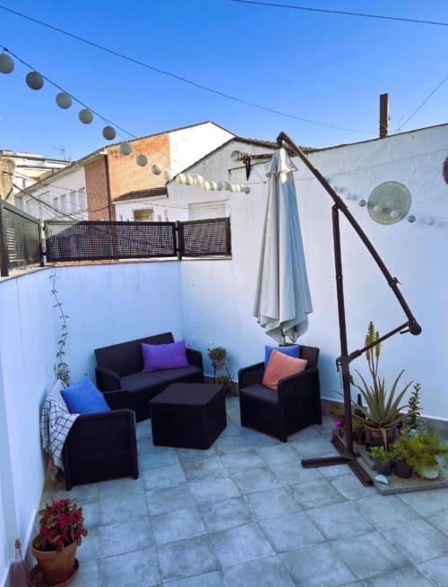 Terraza del apartamento Ohana Arraigo en Mérida con asientos negros, sombrilla y plantas en macetas bajo un cielo despejado