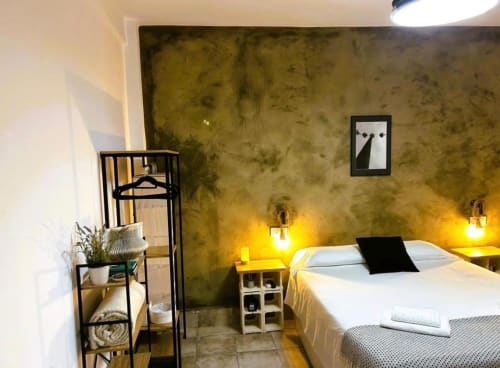 Dormitorio de apartamento en Mérida con paredes texturadas en oliva, cama blanca, iluminación amarilla acentuada y muebles modernos