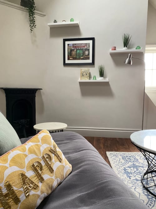 Stylish York apartment bedroom with yellow patterned pillow, gray bedding, white floating shelves with plants, and framed